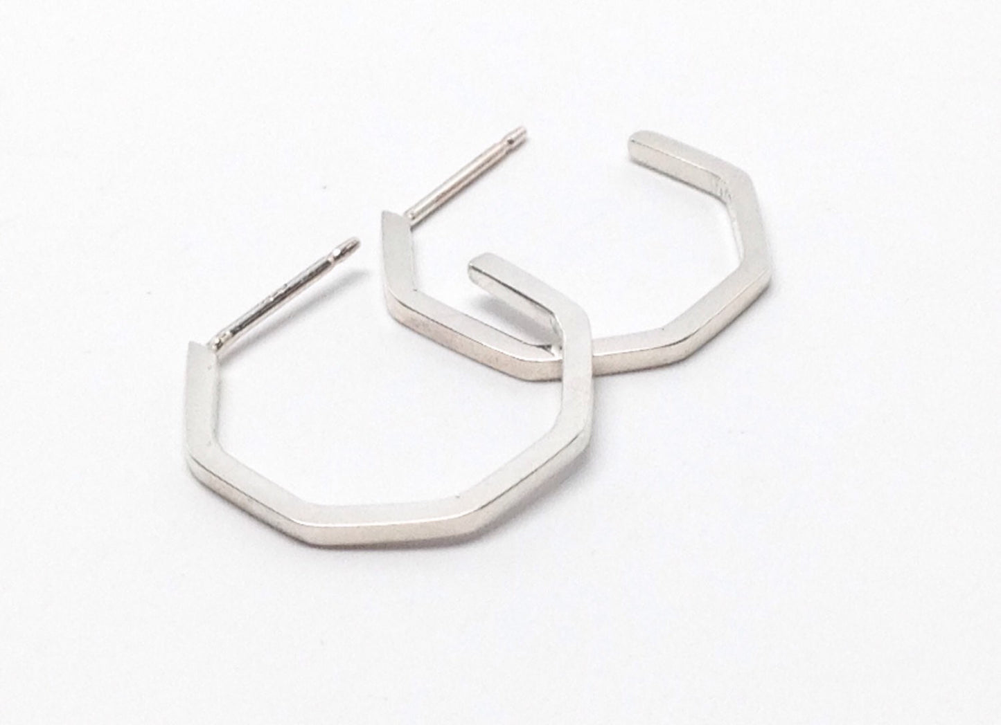 A pair of small sterling silver handmade geometric hoop earrings on a white background