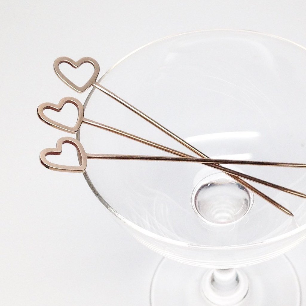 three gold plated heart cocktail picks in clear glass on a white background 