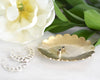 A scalloped edge brass jewelry dish holding stud earrings with silver hoops beside the dish and florals in the background