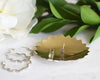 Brass point edged jewelry dish holding silver studs earrings with silver hoops and greenery in the background 